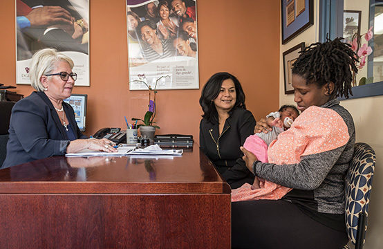 Woman holding an infant sitting with two other women at a office desk