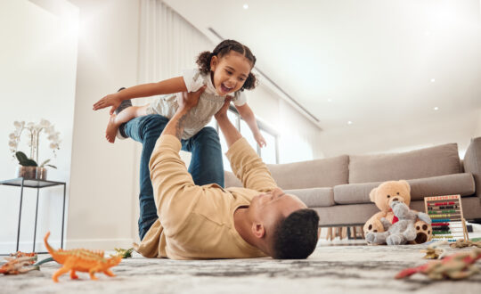 Happy family, father and girl playing in a house with freedom, bonding and enjoying quality time together. Happiness, smile and child flying in dads arms on the floor on a weekend at home in Portugal.
