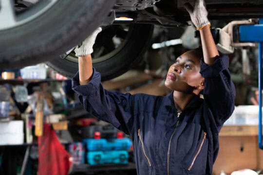 African female mechanic fixing underneath car