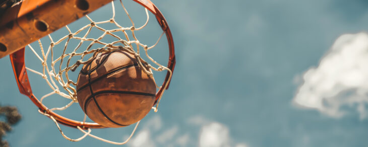 A basketball scores in the net against a clear sky.